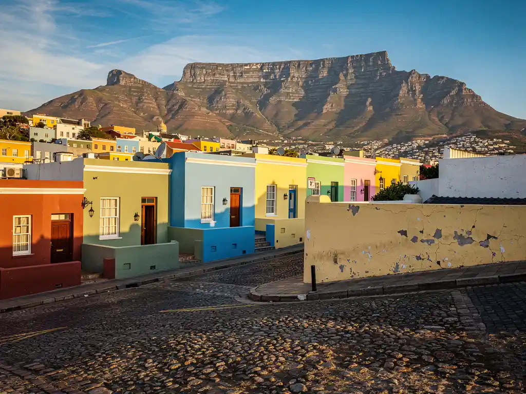 Kleurrijke pastelgevels van Bo-Kaap langs kasseienstraat met Tafelberg op de achtergrond onder strakblauwe lucht, Kaapstad.