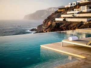 Infinity pool met uitzicht op de turquoise Atlantische Oceaan bij een luxe resort op Kaapverdië, met witte kliffen en een zonnebed in gouden middaglicht.