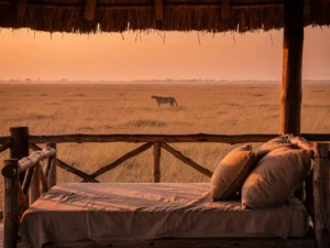 Luxe safarilodge veranda met rieten dak en linnen daybed, uitkijkend over gouden savanne bij zonsondergang met gesilthouetteerde cheetah.