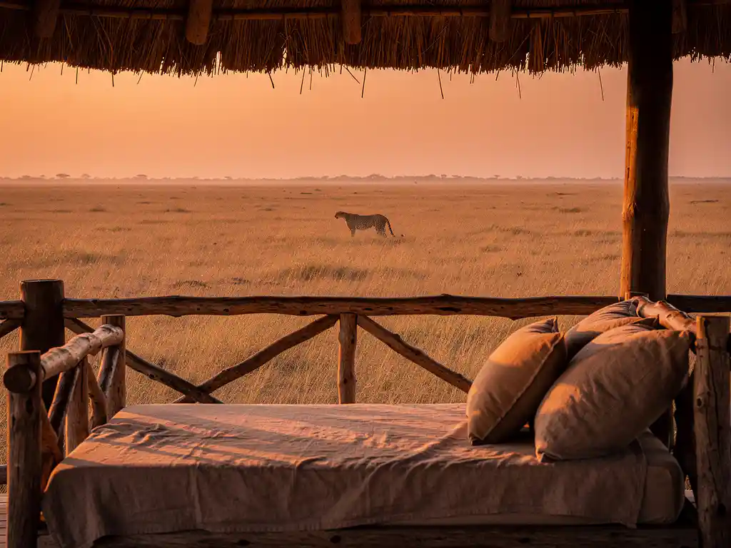 Luxe safarilodge veranda met rieten dak en linnen daybed, uitkijkend over gouden savanne bij zonsondergang met gesilthouetteerde cheetah.