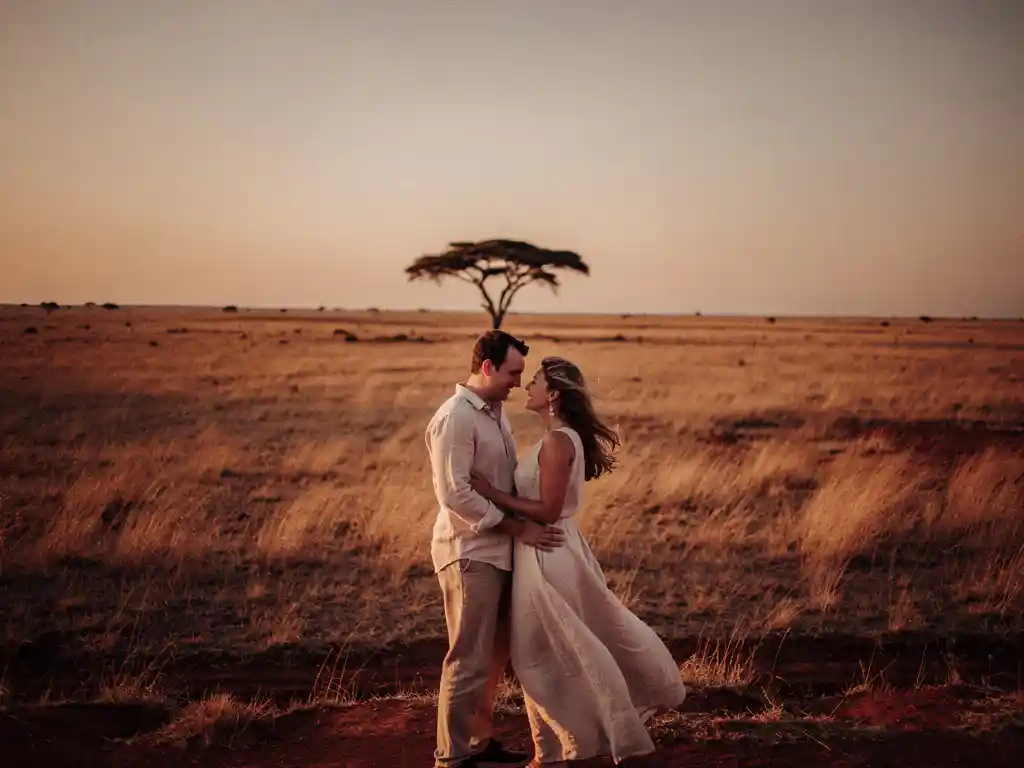 Stel kijkt uit over gouden Zuid-Afrikaanse savanne bij zonsondergang, met silhouet van acacia en warme barnsteentinten.