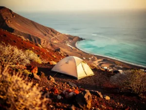 Eenzame tent op vulkanische helling in Kaapverdië met uitzicht op turquoise Atlantische baai tijdens gouden uur.
