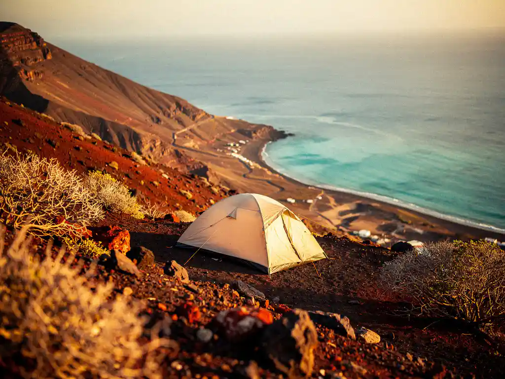 Eenzame tent op vulkanische helling in Kaapverdië met uitzicht op turquoise Atlantische baai tijdens gouden uur.