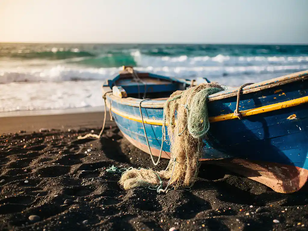 Verweerde houten vissersboot in kobaltblauw en vervaagd geel op zwart vulkanisch strand in Kaapverdië, met droge visnetten over de romp.
