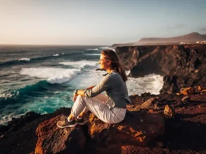 Vrouw zittend op vulkanisch rots aan de kust van Kaapverdië, met turquoise Atlantische golven en gouden middagzon.