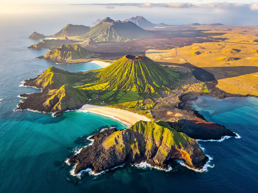 Luchtfoto van vulkanische Atlantische eilanden met turquoise water, basaltrotsen, witte stranden en groene hoogvlakten in gouduur licht.