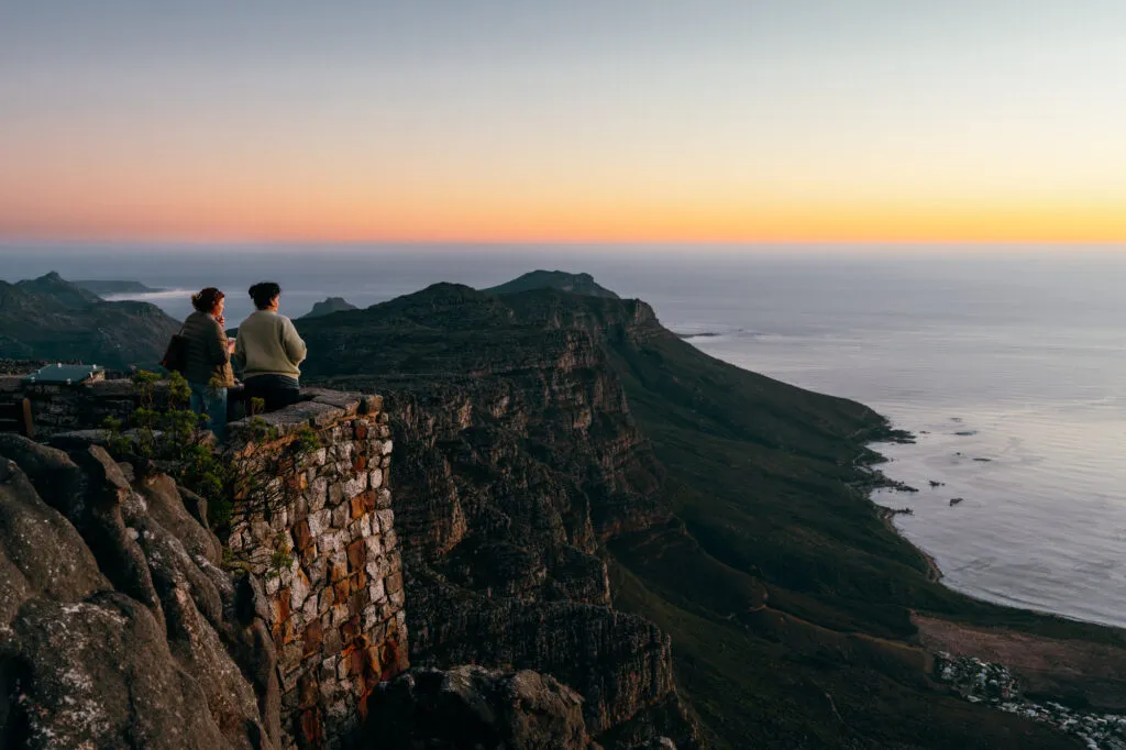 Twee vrouwelijke reizigers kijken vanaf de top van de Tafelberg hoe de zon in zee zakt