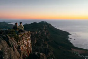Twee vrouwelijke reizigers kijken vanaf de top van de Tafelberg hoe de zon in zee zakt