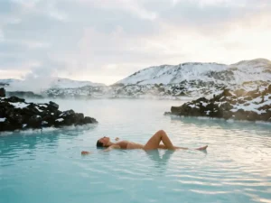 Bader drijft in turquoise geothermaal water van de Blue Lagoon, omringd door besneeuwde lavastenen en opstijgende stoom in IJsland.