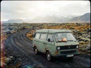 Verweerde campervan op IJslandse lavaweg, omgeven door met mos begroeide lavavelden en besneeuwde bergen, met lunchpakket op de motorkap.