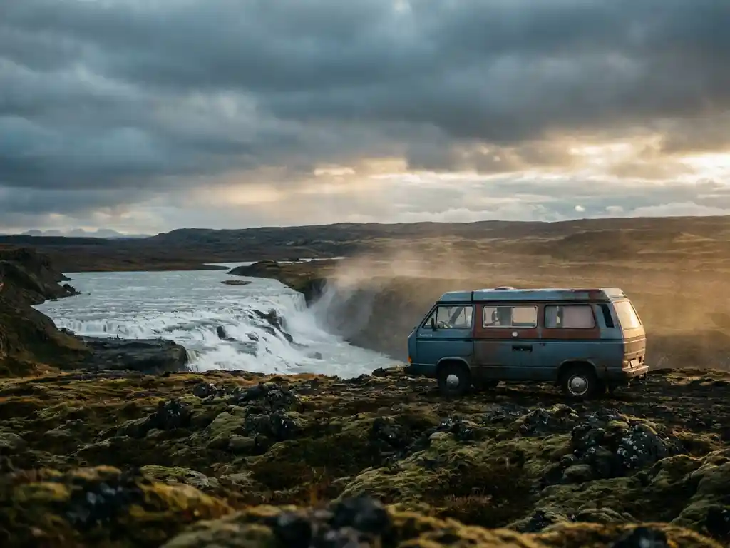 Campervan geparkeerd op bemost lavaveld naast IJslandse waterval, dramatische zwarte vulkanische rotsen onder goudkleurig licht.