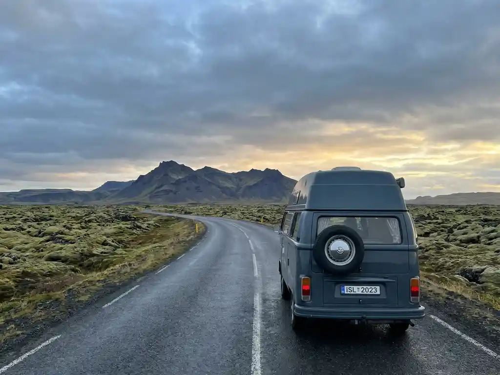 Campervan op IJslands Ring Road omgeven door mosrijke lavavelden en een dramatisch vulkanisch landschap onder bewolkte hemel.