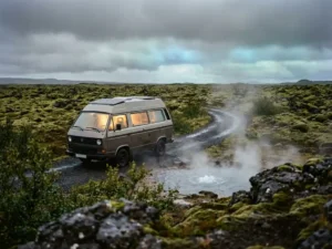Elektrische campervan geparkeerd bij dampende geothermische bron in IJslands vulkanisch landschap met mosgroene lavavelden onder bewolkte lucht.