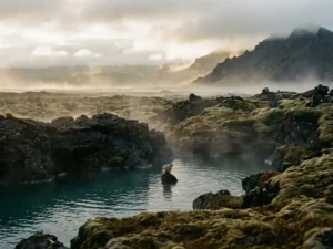 Reiziger ontspant in dampende geothermische warmwaterbron omgeven door zwart vulkanisch gesteente en met mos bedekte lavavelden in IJsland.