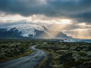 Snæfellsjökull-gletsjer op een stratovulkaan boven zwarte lavavelden, met een smalle kustweg en de Atlantische Oceaan op de achtergrond.