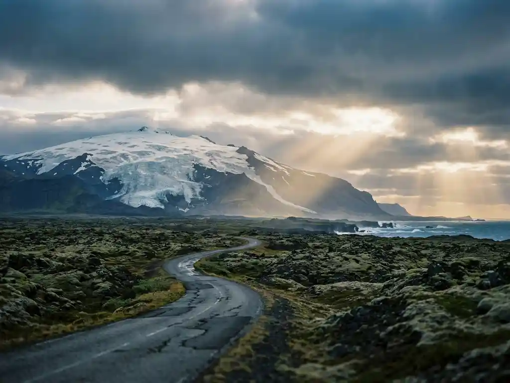 Snæfellsjökull-gletsjer op een stratovulkaan boven zwarte lavavelden, met een smalle kustweg en de Atlantische Oceaan op de achtergrond.