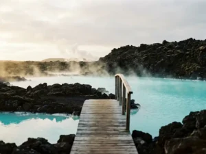 Dampende geothermische hete bron met turquoiseblauw water, omringd door zwart vulkanisch lavagesteente in IJsland, met houten loopbrug.