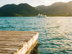 Verouderde houten steiger reikt uit over turquoise Caribisch water bij Martinique, met weelderige vulkanische heuvels en een veerboot op de achtergrond.