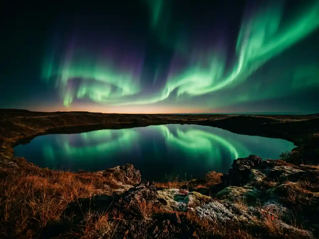 Groen en violet noorderlicht boven IJslands vulkanisch meer, weerspiegeld in het stille water, roestige toendra op de voorgrond.