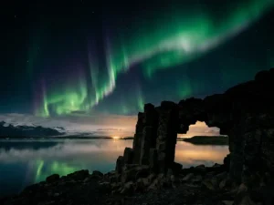 Groen en violet noorderlicht boven IJslands glaciaal lagune, weerspiegeld in spiegelglad water met vulkanische basaltkolommen op de voorgrond.