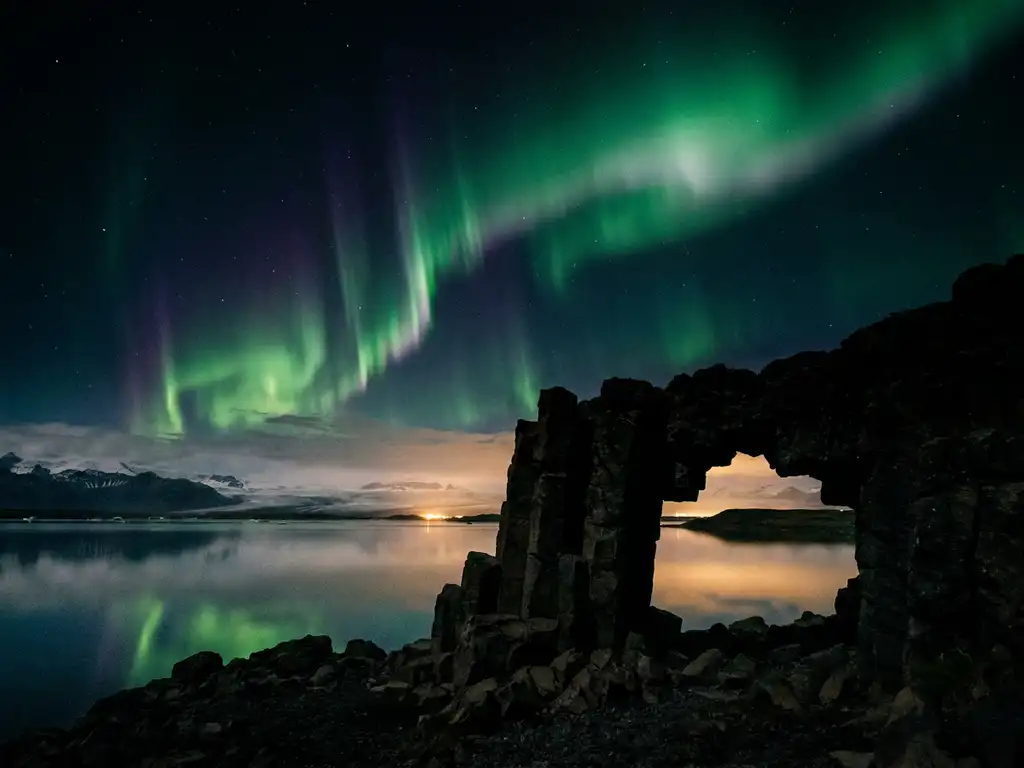 Groen en violet noorderlicht boven IJslands glaciaal lagune, weerspiegeld in spiegelglad water met vulkanische basaltkolommen op de voorgrond.