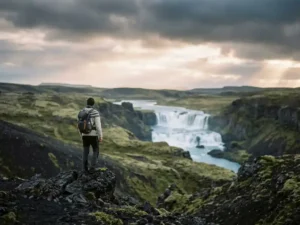 Reiziger aan de rand van IJslands vulkanisch landschap met waterval in de verte onder arctisch licht.