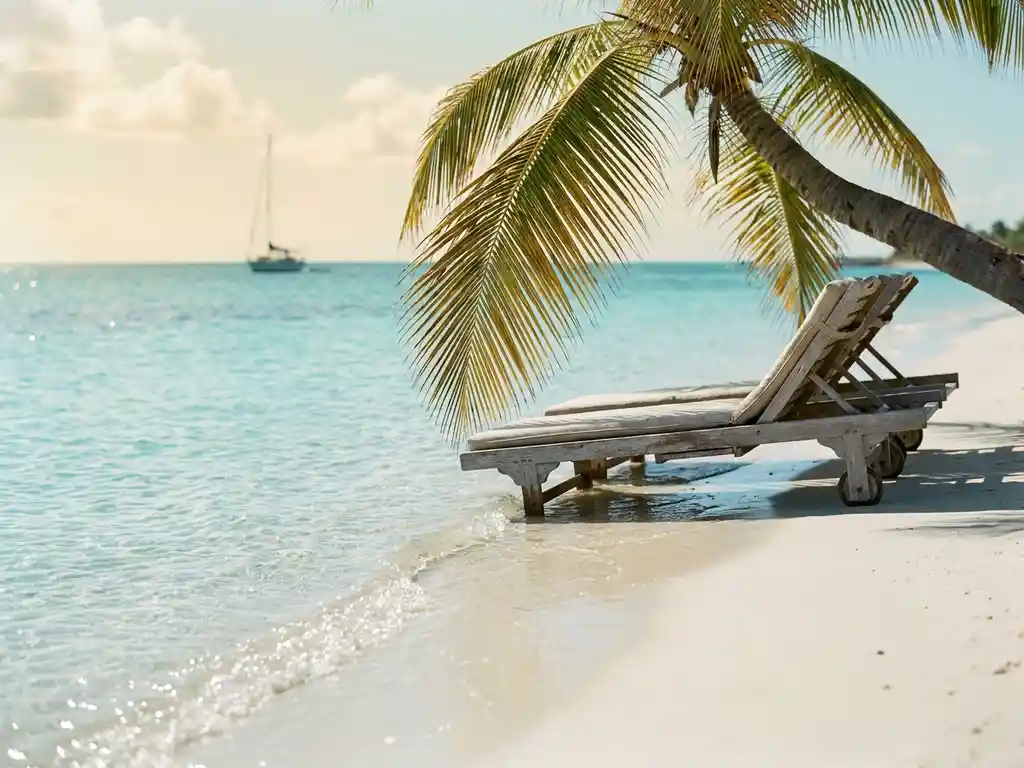 Turquoise baai op Saint-Martin met poederwit zand, een houten ligstoel in de schaduw van een palmboom en kalm Caribisch water.