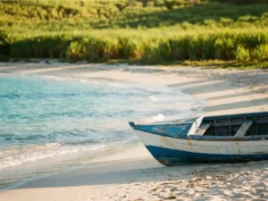 Verlaten wit zandstrand op Marie-Galante met turquoise Caribisch water, houten visserboot op het zand en suikerrietvelden op de achtergrond.