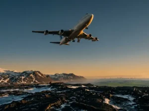 Vliegtuig boven IJslands vulkanisch landschap met zwarte lavavelden, besneeuwde bergen en een gouden arctische horizon.