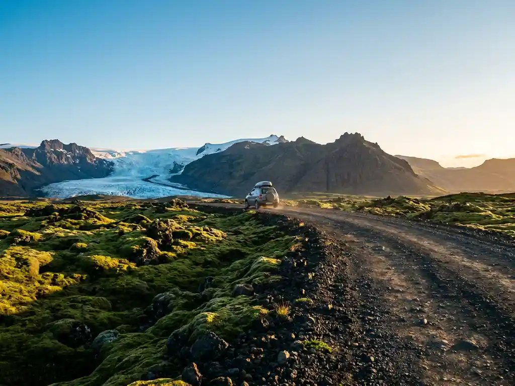 Grindweg slingerend door IJslands zomerlandschap met gletsjer, vulkanische bergen, en smaragdgroen mos onder middernachtzon.