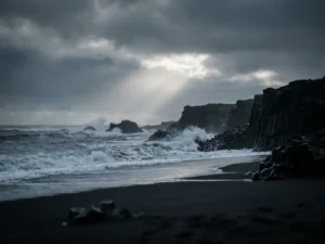 Zwart zandstrand in IJsland met krachtige Atlantische golven, vulkanische basaltrotsen en een dramatische bewolkte lucht met zilver licht.