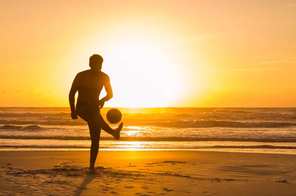 Een lokale man voetbalt op een zonnig zandstrand; de ware passie voor Kaapverdië voetbal.