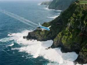 Commercieel vliegtuig boven de vulkanische kustlijn van de Azoren met dramatische Atlantische golven en groene kliffen.