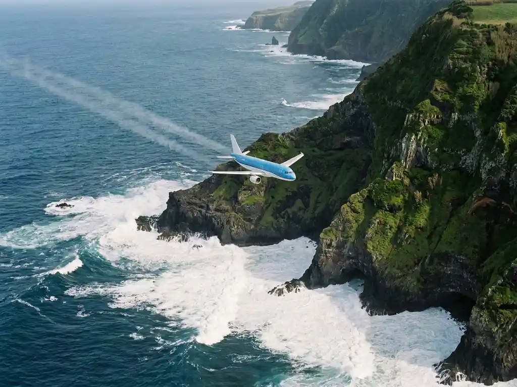 Commercieel vliegtuig boven de vulkanische kustlijn van de Azoren met dramatische Atlantische golven en groene kliffen.